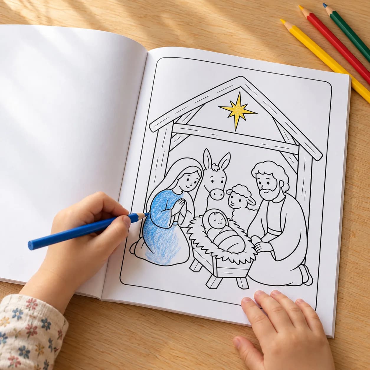 A child’s hands coloring the nativity page of the open paperback with a blue pencil, with colored pencils beside the book.